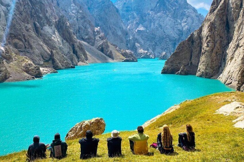 Un grupo de personas sentadas en una colina cubierta de hierba con vistas a un lago turquesa rodeado de montañas rocosas. 3