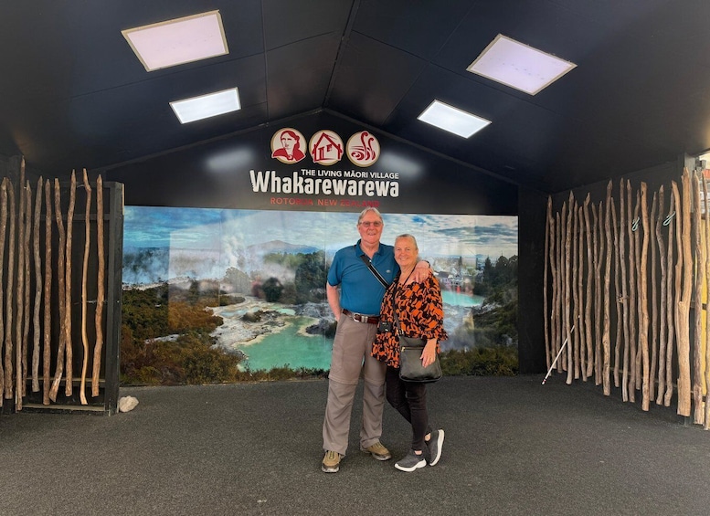 A couple standing in front of a sign for Whakapowewa, with a backdrop of a scenic landscape. 4