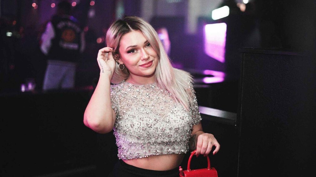 A person wearing a sparkly, sequined top and holding a red handbag. 3