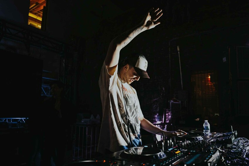 A DJ performing at a club with a raised arm, a water bottle, and a DJ mixer. 5