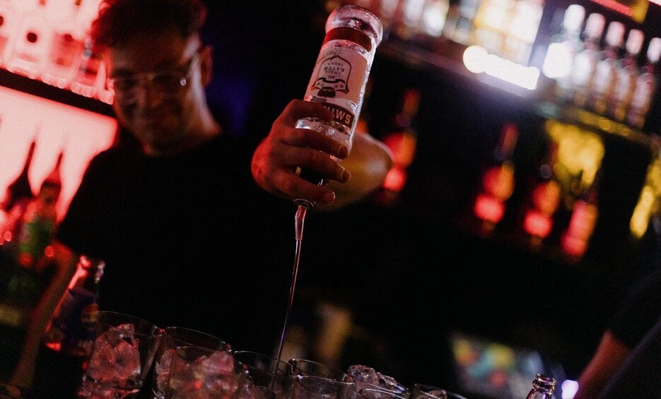 A person pouring a drink from a bottle into a glass. 4