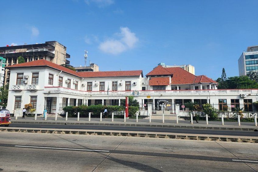 A white building with a red roof and a balcony, located on a street with a sidewalk and a road in front. 3
