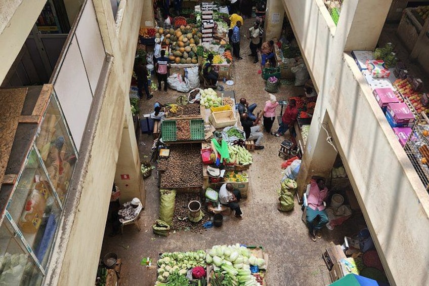 An indoor market with various stalls selling fruits and vegetables. 2