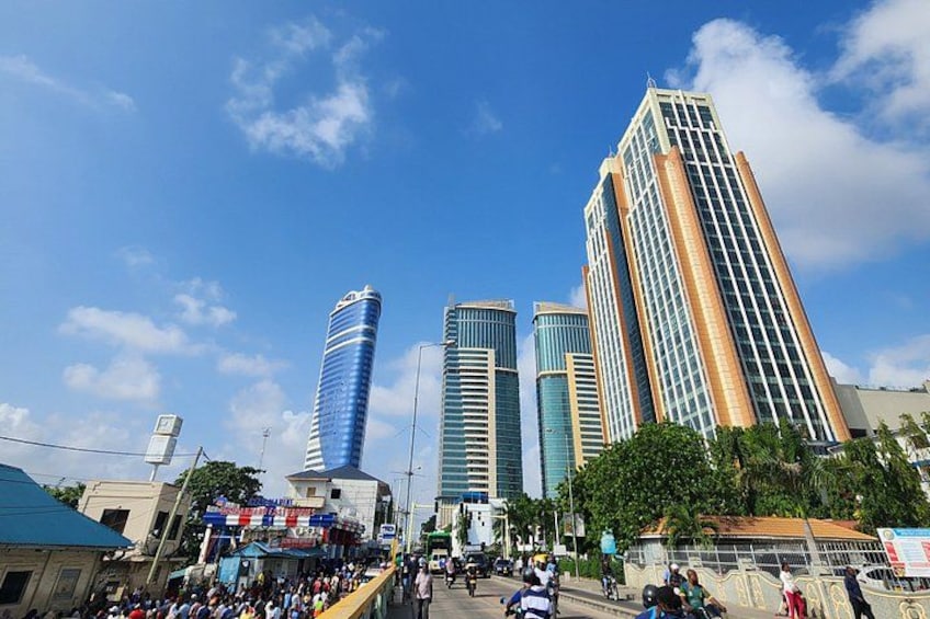 A cityscape with tall buildings, a clear sky, and a busy street with pedestrians and vehicles. 5