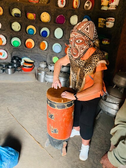 A person playing a drum in a room with various colorful plates and pots on the wall. 2