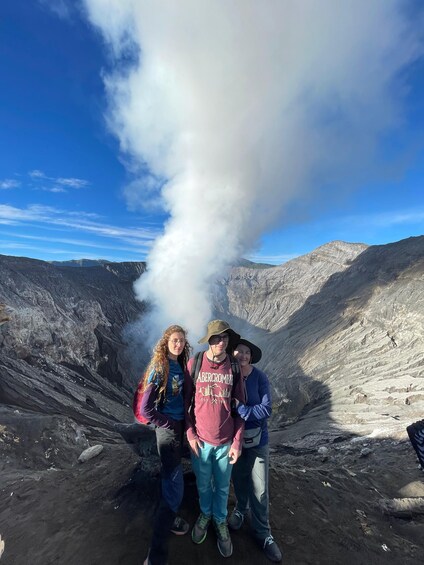 Three people standing near a volcanic vent emitting smoke. 1