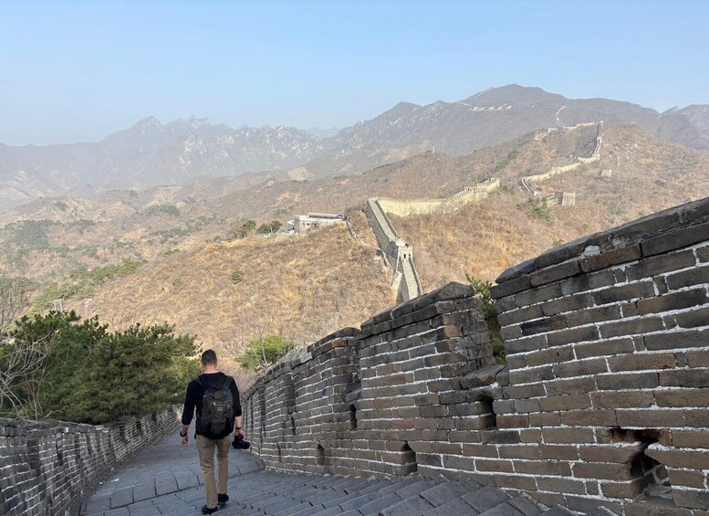 A person walking along the Great Wall of China, with mountains in the background. 1