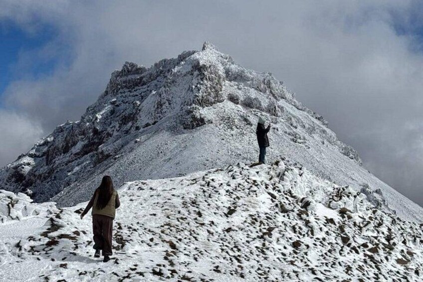 Two people hiking on a snow-covered mountain peak. 4