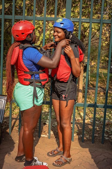 Two people wearing helmets and life vests, standing in front of a metal fence. 5