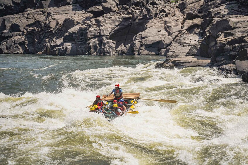 A group of people in a raft navigating through turbulent waters with rocky cliffs in the background. 3