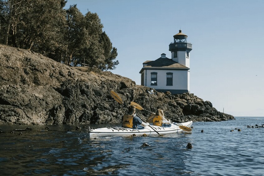 A kayak on a rocky shoreline with a lighthouse in the background. 1