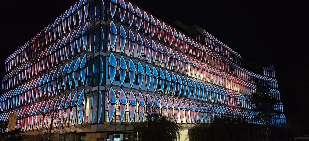 A building with a facade of triangular glass panels illuminated in blue and pink hues. 2