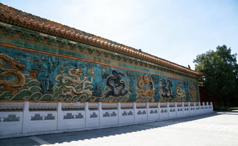 A long wall with intricate dragon murals and a tiled roof. 3