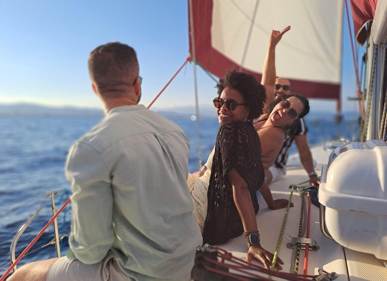 A sailboat with people on deck, a clear sky, and the ocean in the background. 4