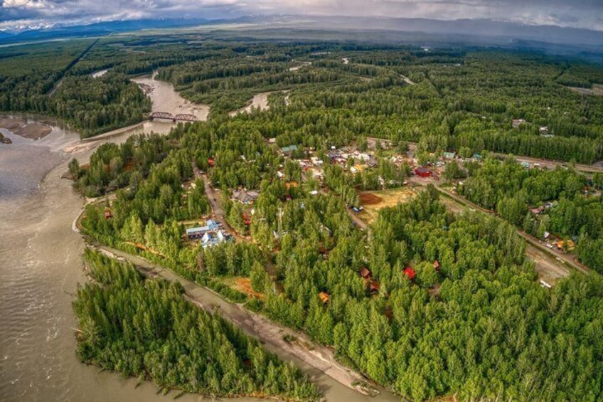 An aerial view of a riverside settlement with dense forests, a bridge, and scattered buildings. 1