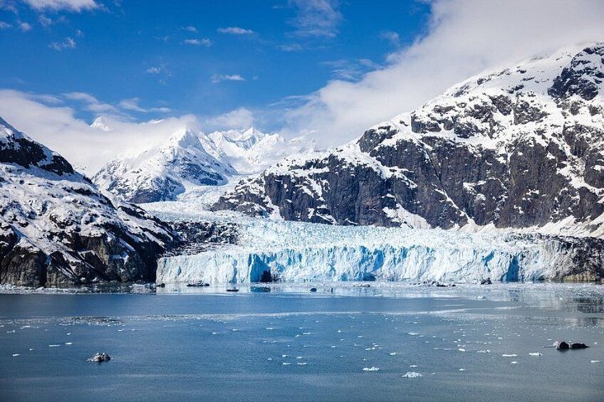 Un glacier dont la face est constituée de glace bleue, entouré de montagnes enneigées et surplomb é d’un ciel dégagé. 3