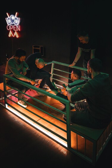 A group of people sitting around a table in a dimly lit room with a neon sign that reads 'OPEN'. 2
