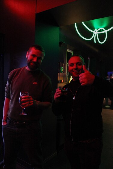 Two people holding drinks in a dimly lit room with a neon sign. 3