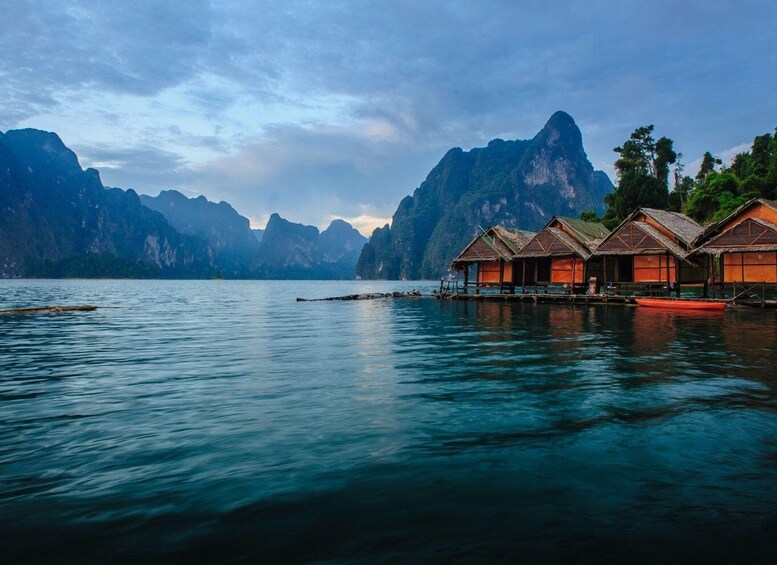 A calm lake with wooden floating houses and a mountainous backdrop. 1