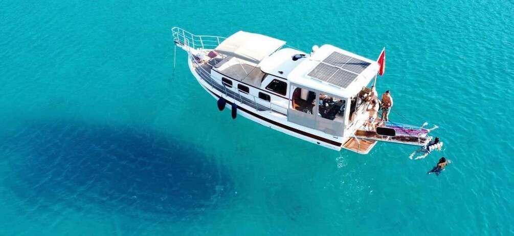 A white boat with a covered deck and a flag, anchored in clear turquoise water. 5