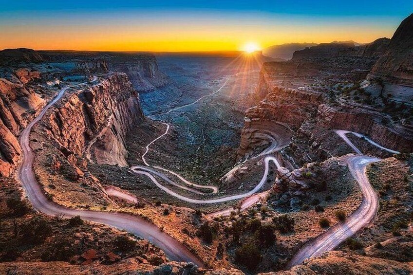 A winding road through a canyon with a sunset in the background. 1