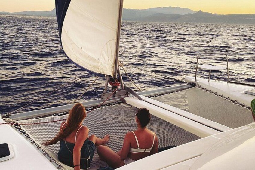 Eine Segelyacht mit zwei Personen an Deck, einem Segel und einem Wassergebiet mit weiter Landansicht. 2
