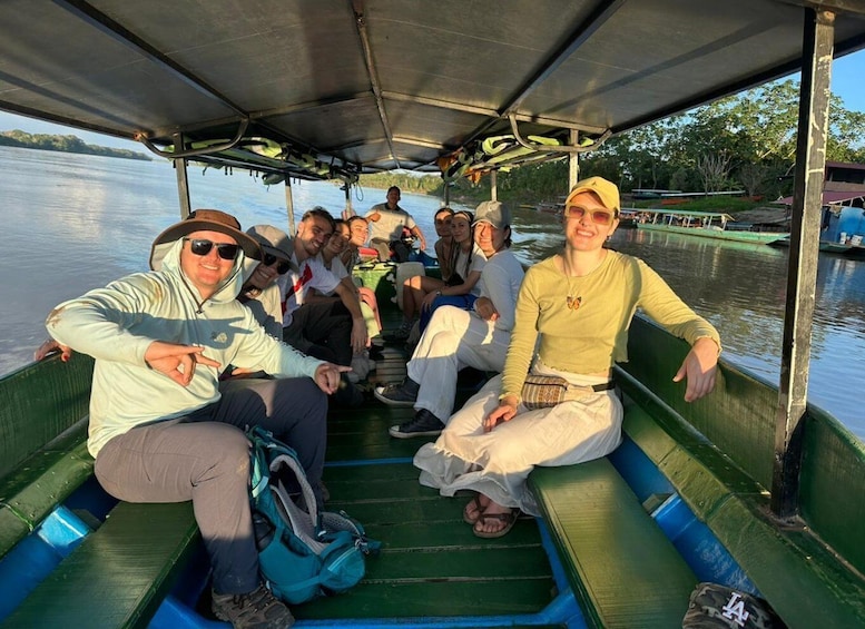 A group of people on a green boat with a metal roof, sitting and enjoying a sunny day on a calm body of water. 2