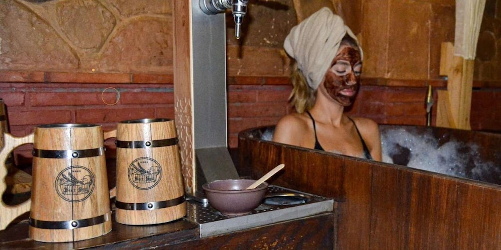 A person in a wooden bathtub with two wooden barrels beside it. 1