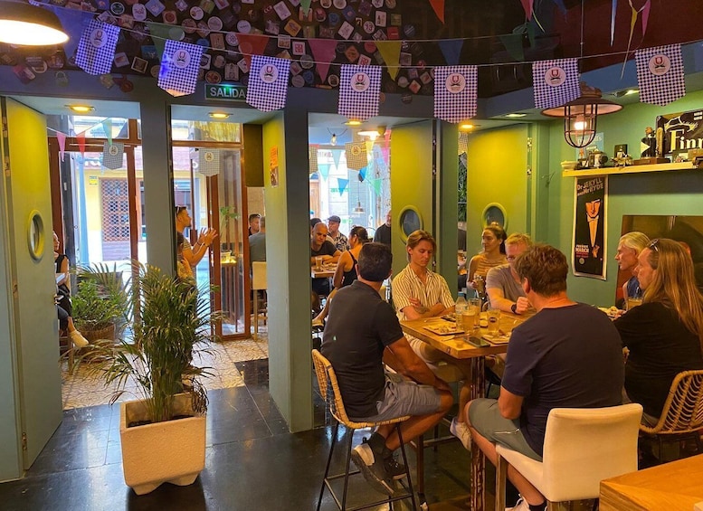 A restaurant interior with patrons dining at tables, decorated with checkered bunting and various posters. 2