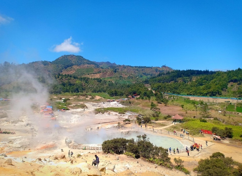 A geothermal area with steam vents, a pool of water, and a mountainous backdrop. 3
