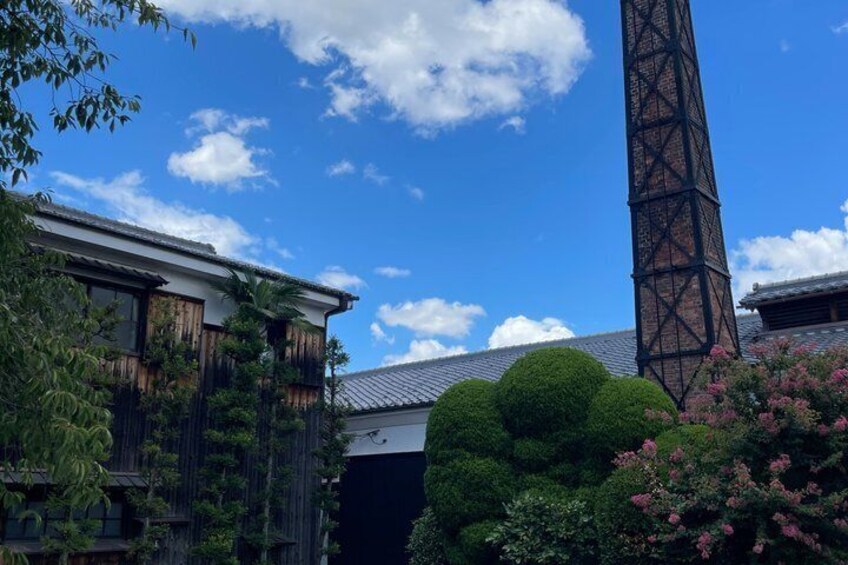 En traditionel japansk bygning med træfacade, et sort metalstårn og frodig vegetation. 2