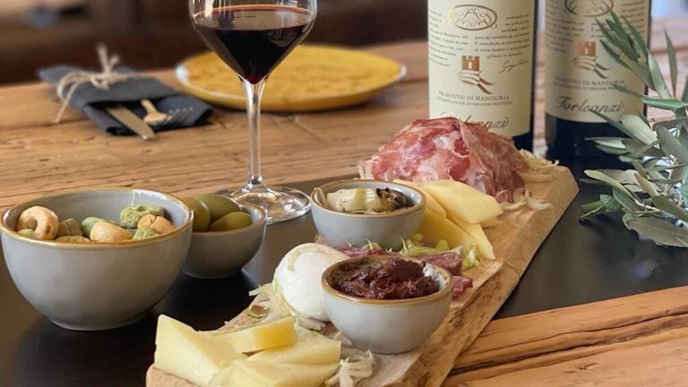 A wooden board with cheese, olives, nuts, and cured meats, accompanied by a glass of red wine. 2