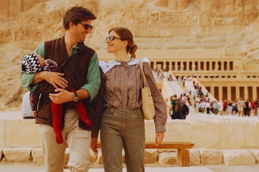 A couple walking near ancient Egyptian ruins with a large crowd in the background. 3