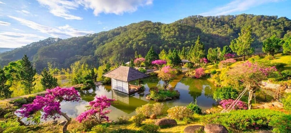 A serene garden with a pond, blooming pink flowers, and a traditional Japanese-style building. 1