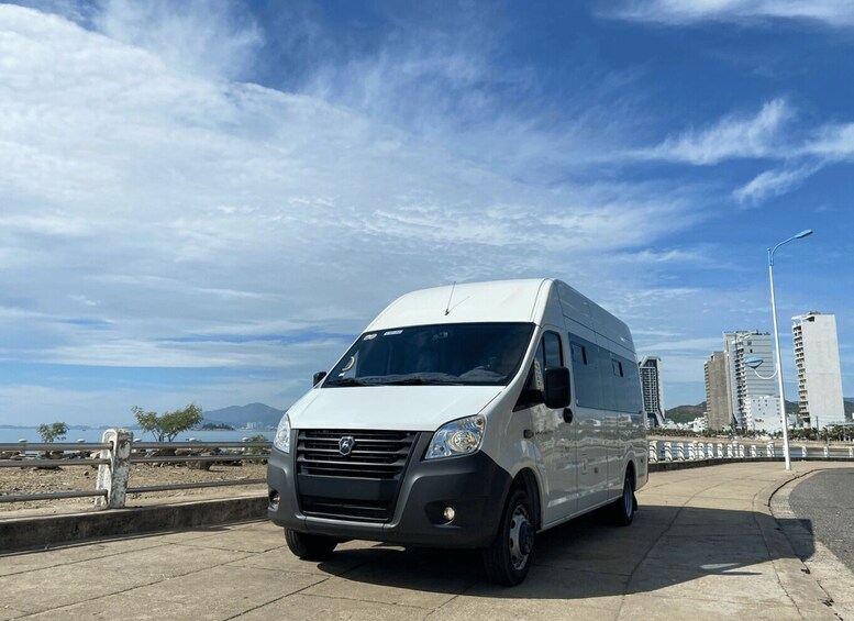 A white van parked on a concrete sidewalk with a cityscape and mountains in the background. 3