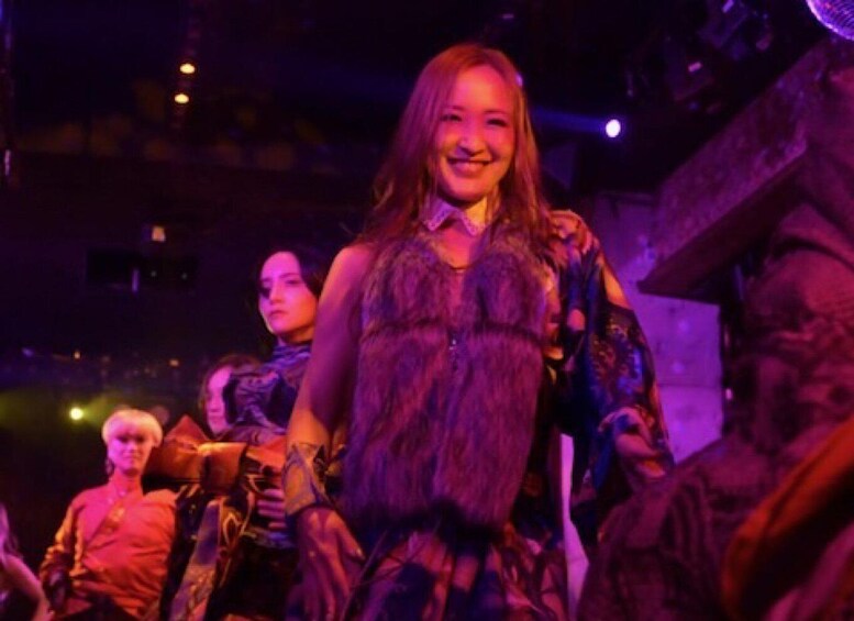 A person in a fur coat at a dimly lit event with stage lighting. 1