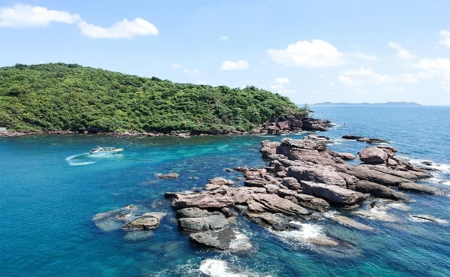 A coastal landscape with clear blue waters, rocky outcrops, and a forested hill. 3