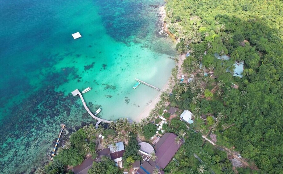 An aerial view of a coastal area with clear turquoise waters, a pier, and a cluster of buildings surrounded by dense greenery. 5