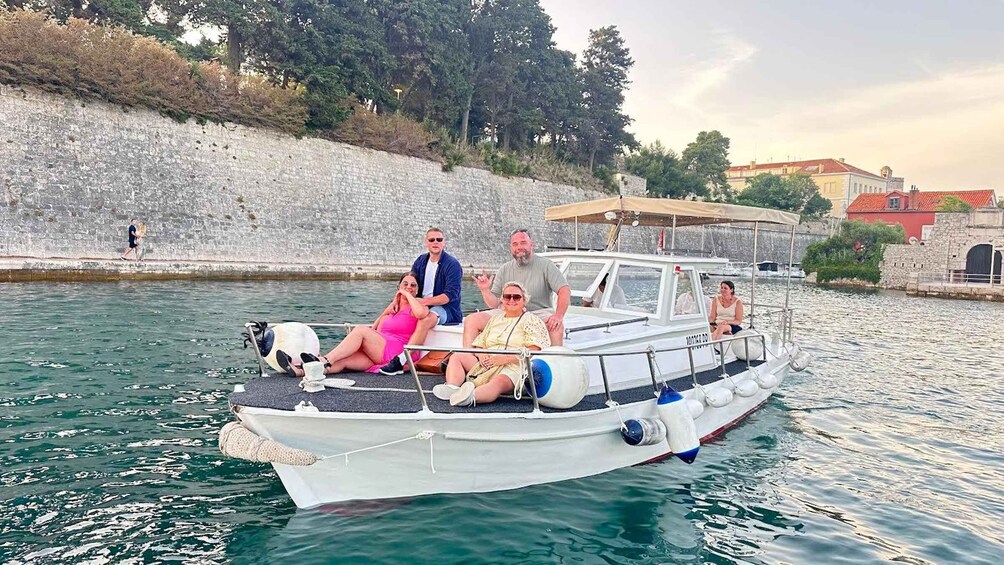 A group of people on a boat in a calm body of water, with a stone wall and buildings in the background. 3