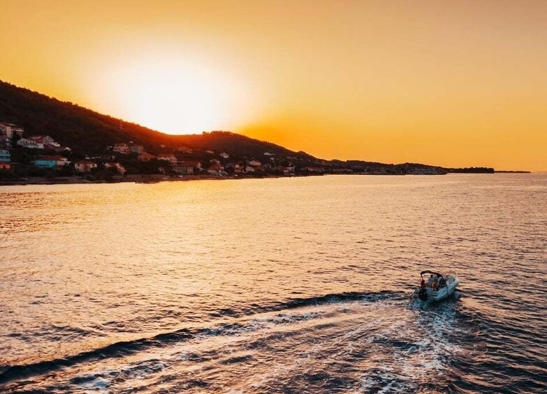 A boat on calm water during sunset with a sunlit coastline and hills in the background. 4