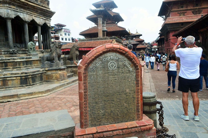 A historical monument with inscriptions, surrounded by traditional architecture and a crowd of visitors. 4
