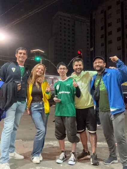 A group of people posing for a photo at night with a traffic light and buildings in the background. 5