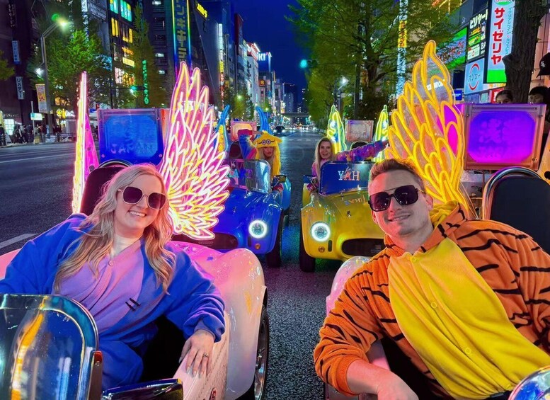 Two people in a brightly lit urban street with neon signs and vehicles. 1