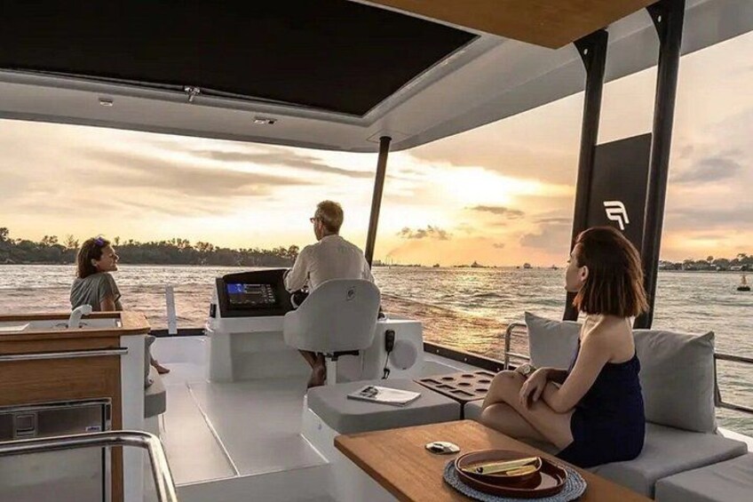 A boat with two people on deck, a woman in a white shirt and a woman in a blue dress, with a sunset in the background. 4