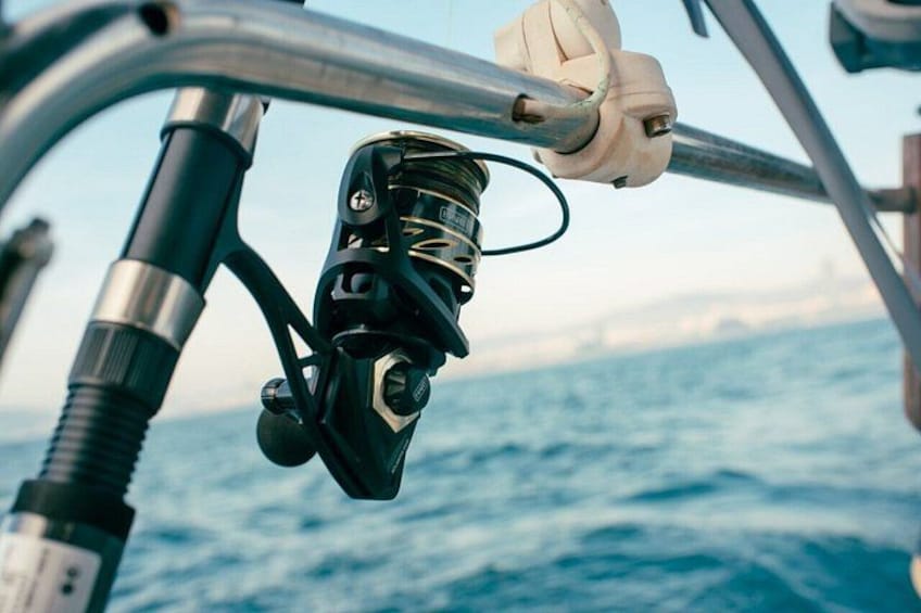 A fishing rod with a reel and line, a white glove, and a metal handle, all on a boat with a view of the ocean. 2