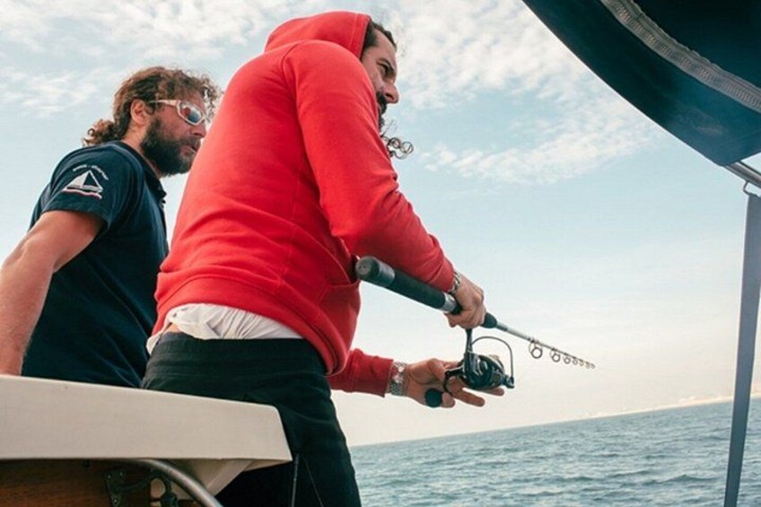 Two people fishing on a boat with a calm sea and a clear sky in the background. 3