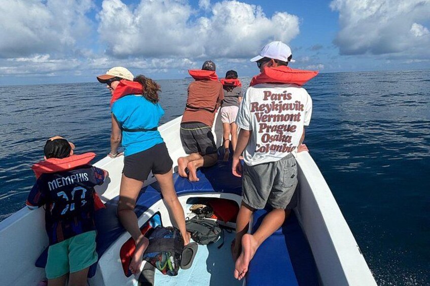 Un grupo de personas en un bote, usando chalecos salvavidas, algunas con gorras que tienen texto en la parte de atrás. 2