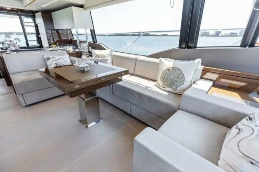 A modern yacht interior with a dining area, sofas, and a view of the water. 5