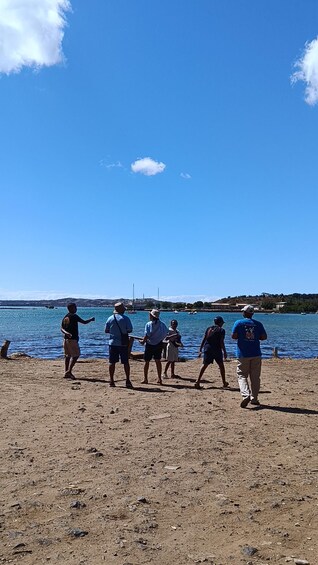 En gruppe mennesker på en sandstrand med en klar blå himmel og stille hav. 5