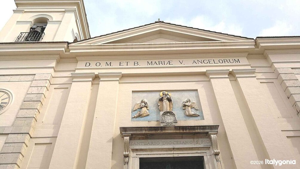 A building facade with a clock, a plaque with inscriptions, and a statue of the Virgin Mary. 3
